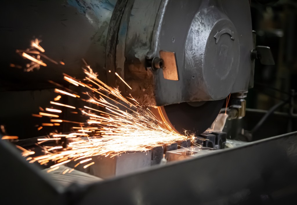 Abrasive cutoff saw producing sparks while cutting metal stock.