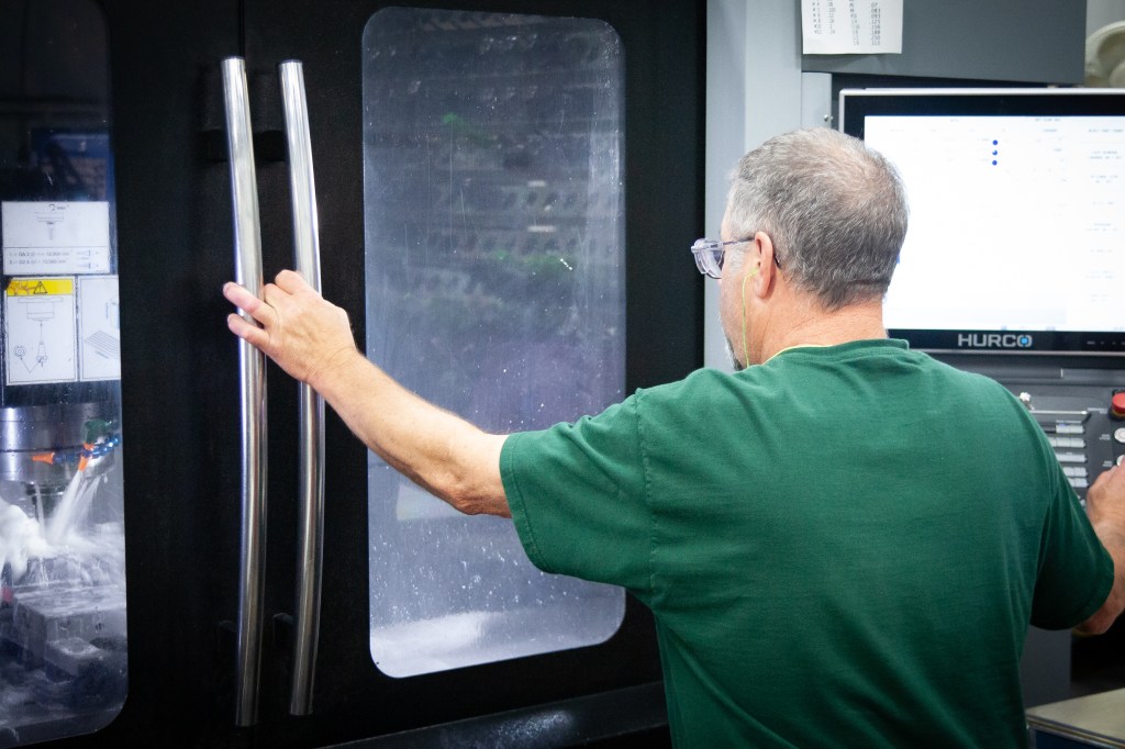 Machinist operating a Hurco CNC machine from the control panel.