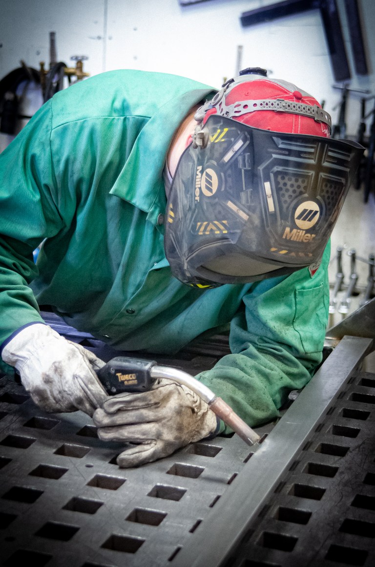 Welder fabricating a metal assembly at a fixture table.