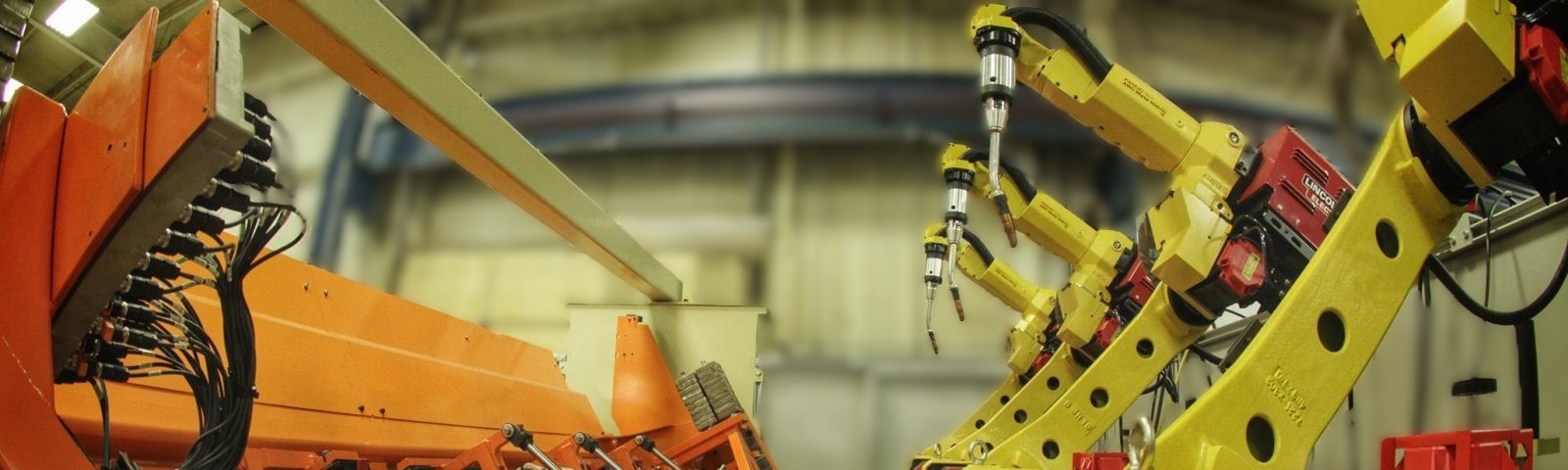 Industrial robotic welding arms positioned inside a guarded automation cell.
