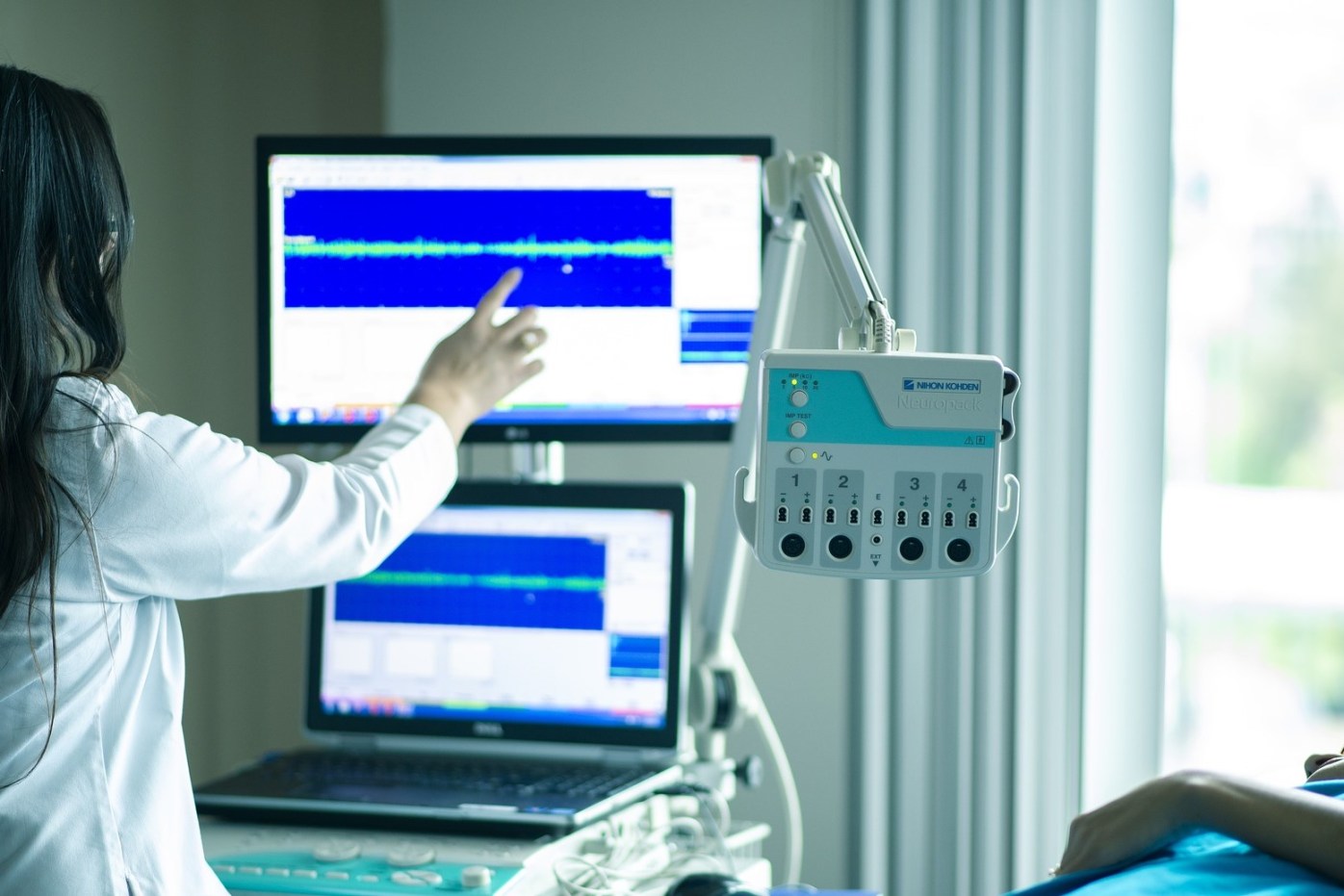 Medical professional reviewing diagnostic waveforms beside patient-monitoring equipment