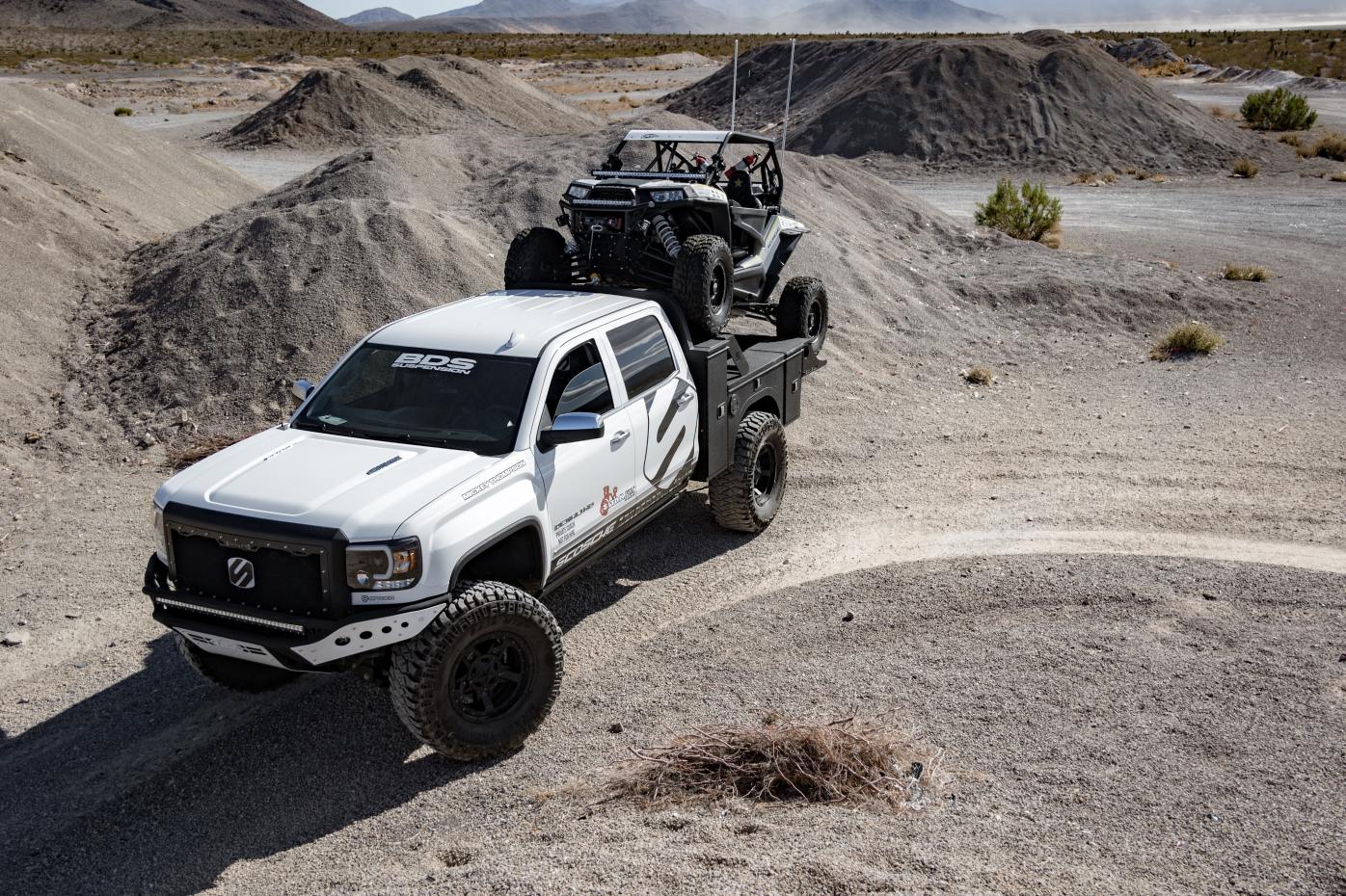 Off-road pickup carrying a utility terrain vehicle through a gravel course