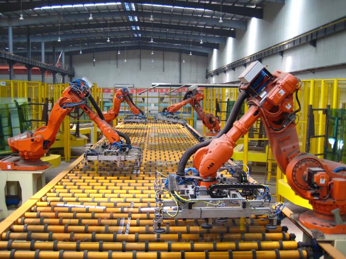 Industrial robots transferring material across a roller conveyor line